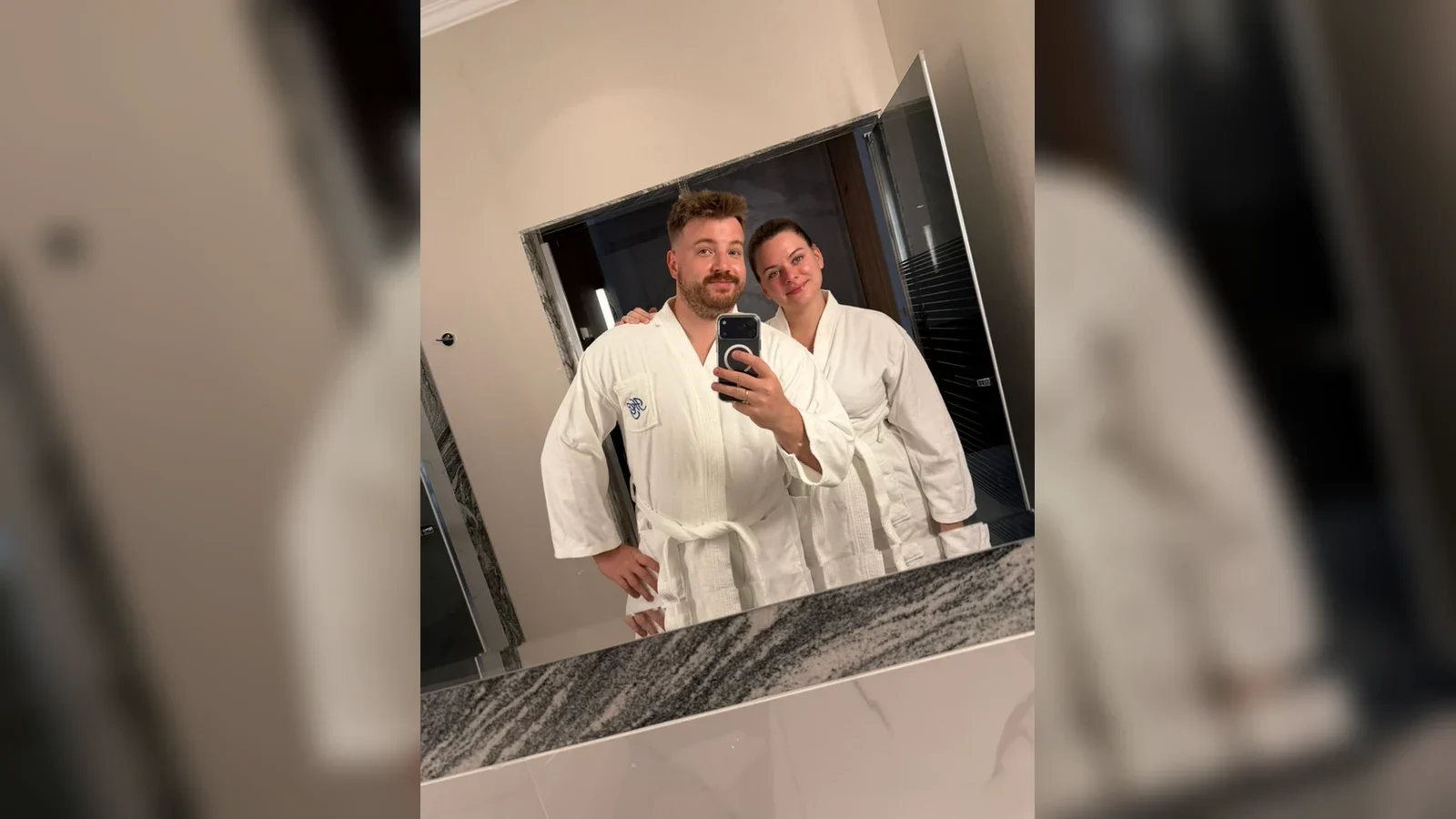 Para gości w szlafrokach robi zdjęcie w lustrze łazienki w pokoju Hotelu Gołębiewski w Pobierowie.