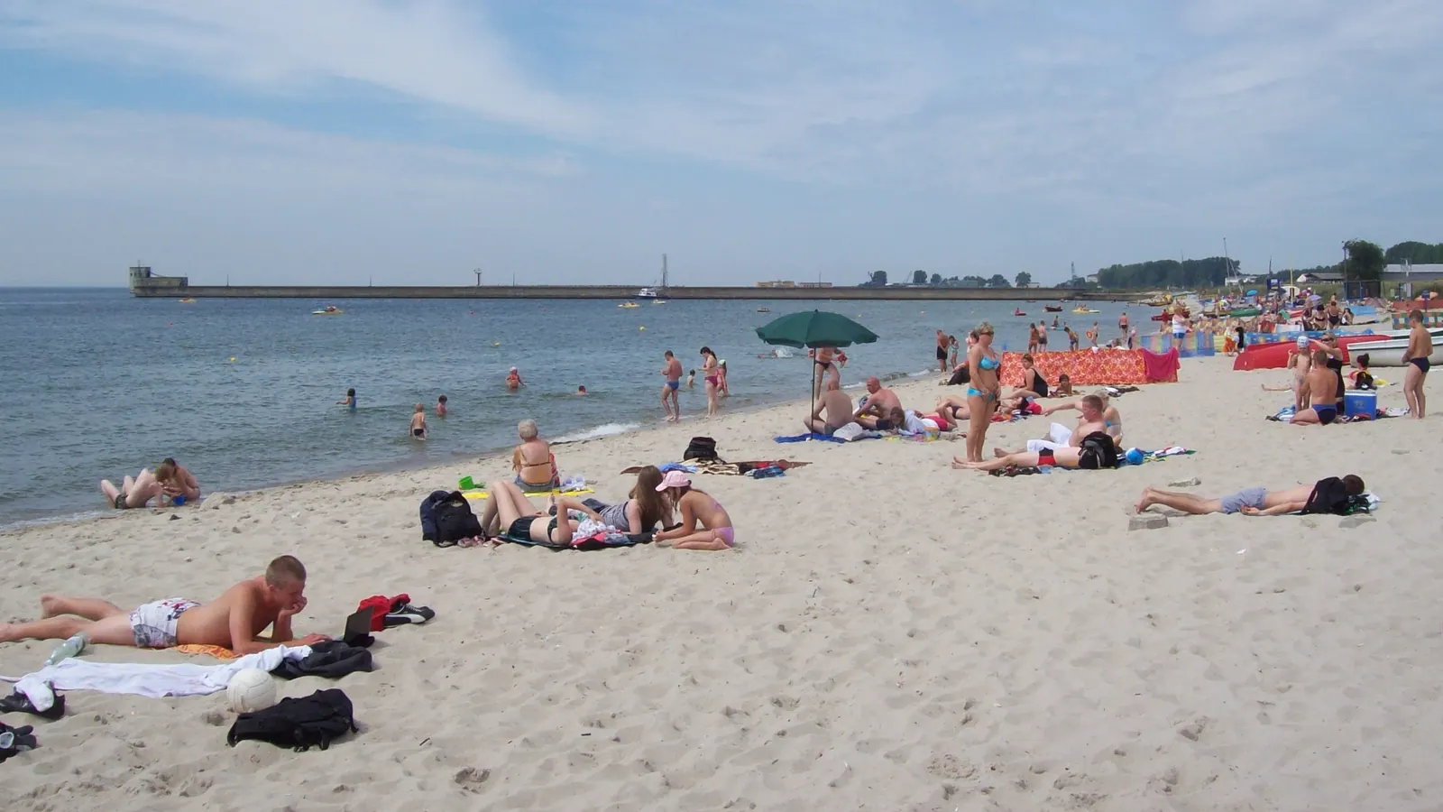 Plaża w Helu z jasnym piaskiem, turystami i widokiem na wodę.