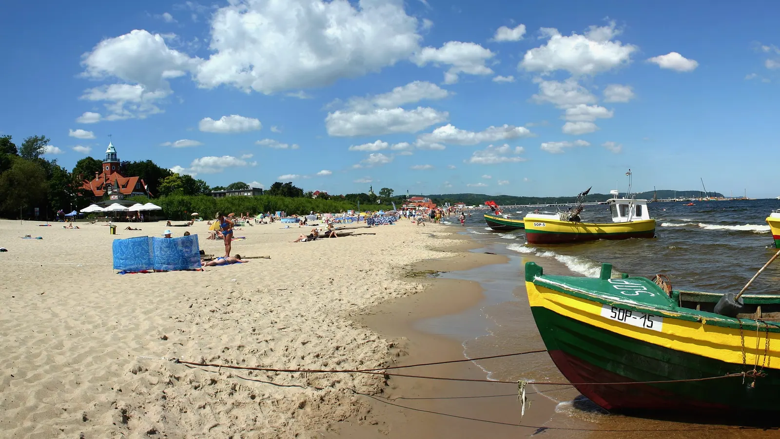 Plaża w Sopocie z łodziami, jasnym piaskiem i zabudową kurortu w tle.