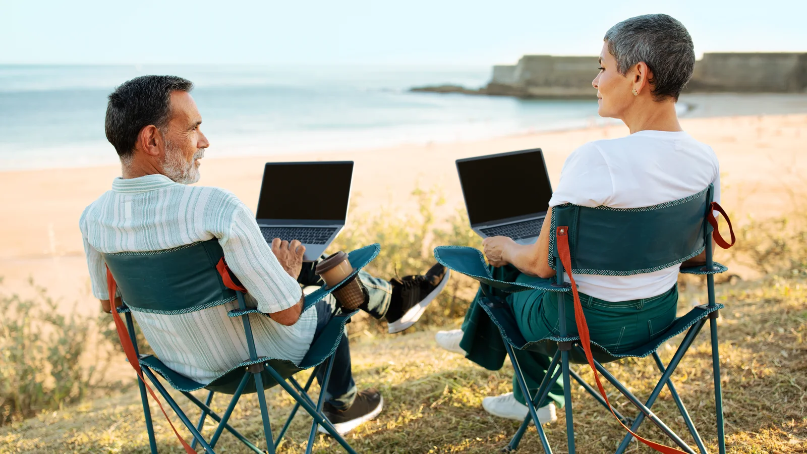 Para pracująca na laptopach na składanych krzesłach z widokiem na ocean.
